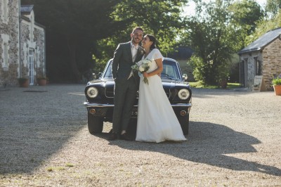 Robe de mariée en dentelle suspendue devant une fenêtre lumineuse avec vue sur un jardin verdoyant.