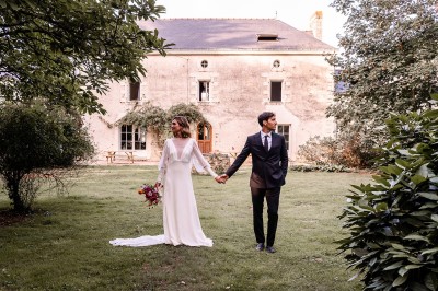 Robe de mariée en dentelle suspendue devant une fenêtre lumineuse avec vue sur un jardin verdoyant.