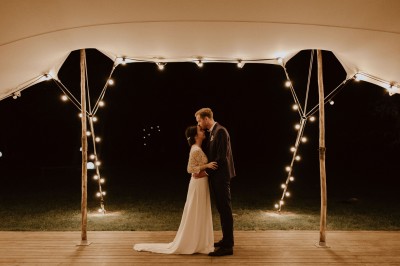 Robe de mariée en dentelle suspendue devant une fenêtre lumineuse avec vue sur un jardin verdoyant.