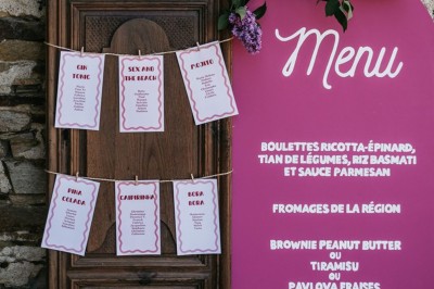 Robe de mariée en dentelle suspendue devant une fenêtre lumineuse avec vue sur un jardin verdoyant.