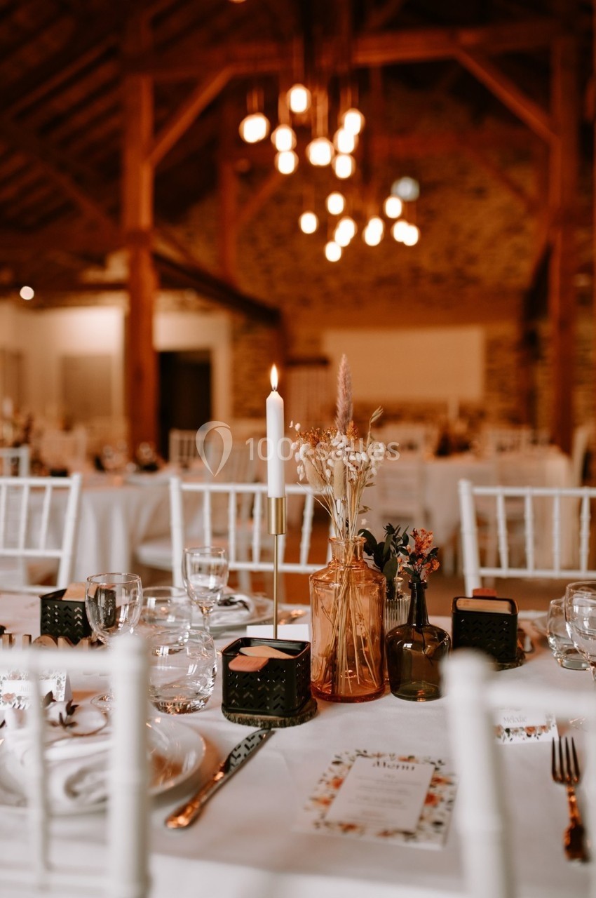 Salle de réception décorée avec des tables dressées, bougies allumées et fleurs séchées dans un cadre rustique.