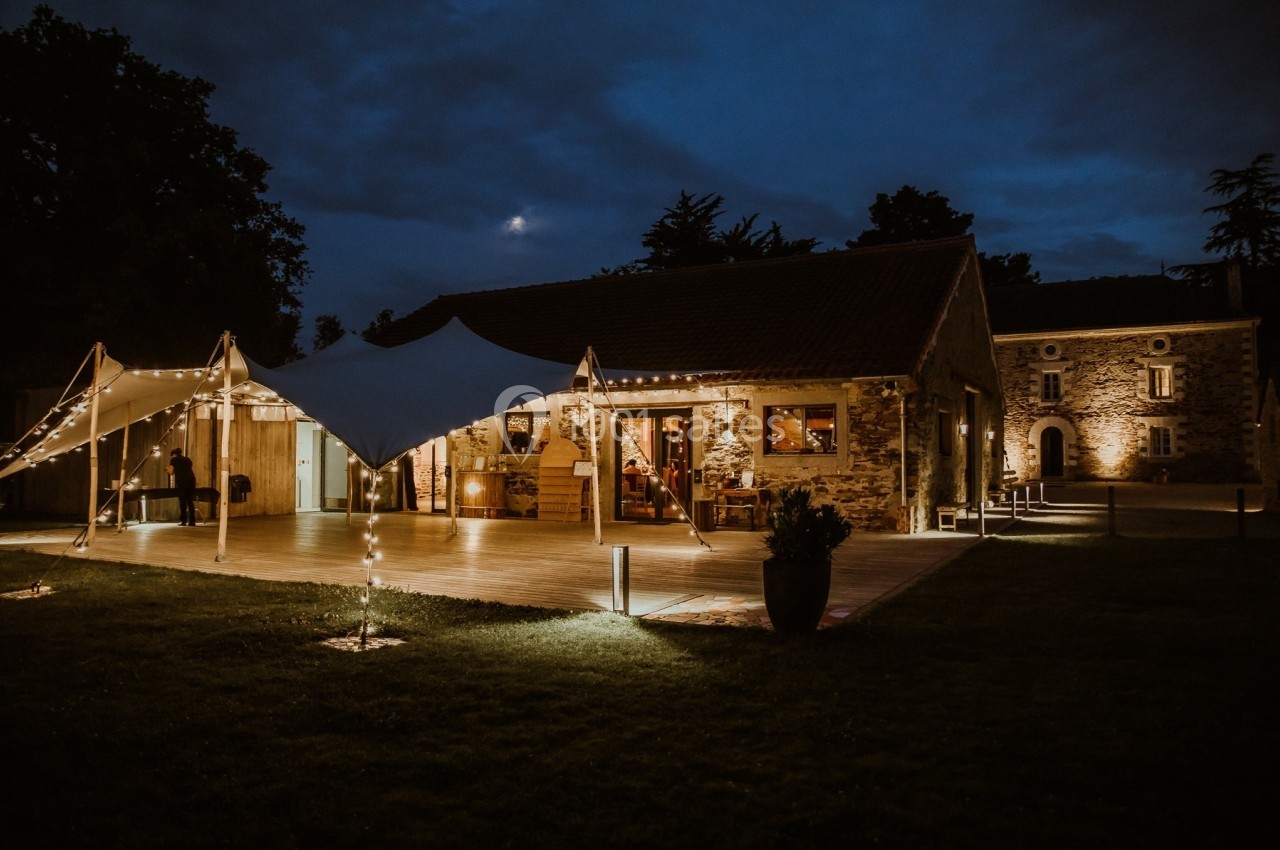 Bâtiment en pierre éclairé de nuit avec une tente lumineuse installée sur une terrasse en bois.