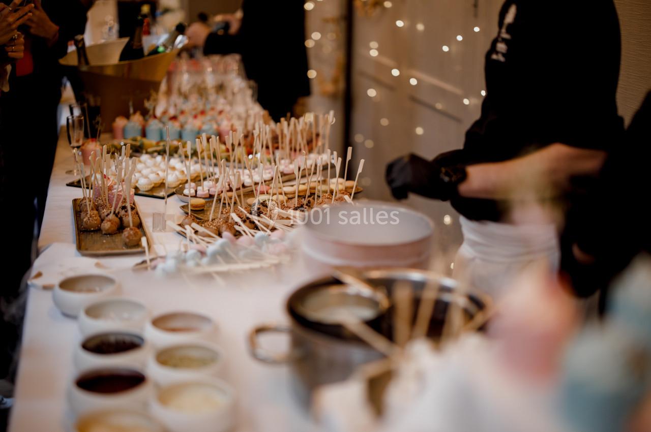 Table garnie de brochettes sucrées, sauces et desserts, avec un décor lumineux en arrière-plan.