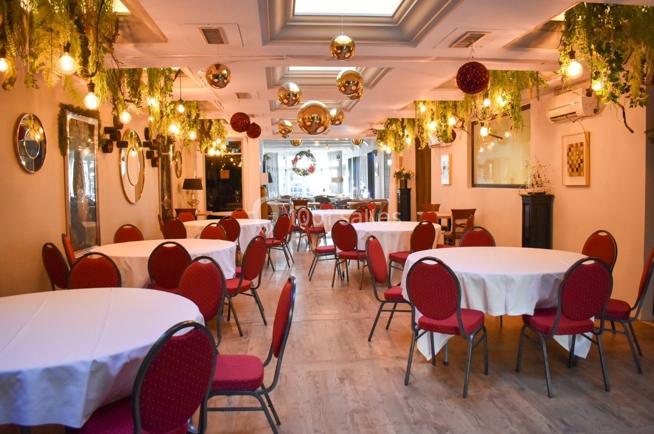 Salle de réception décorée avec des tables rondes, des chaises rouges, des guirlandes lumineuses et des plantes suspendues.
