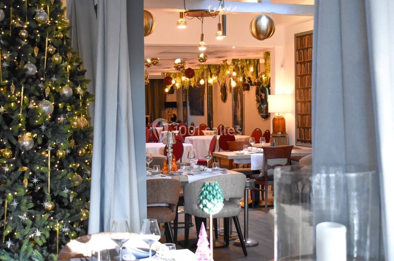 Salle de restaurant décorée pour Noël avec sapin illuminé, guirlandes suspendues et tables dressées.