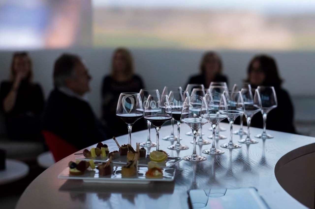 Verres de vin alignés sur un comptoir avec des amuse-bouches au premier plan et des personnes floues en arrière-plan.