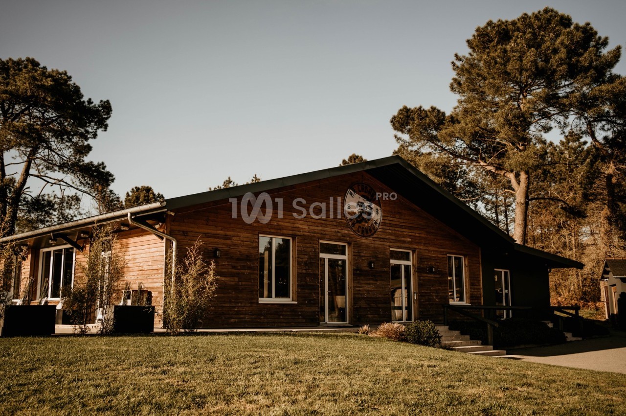 Bâtiment en bois entouré de végétation, avec une pelouse au premier plan et des arbres en arrière-plan.