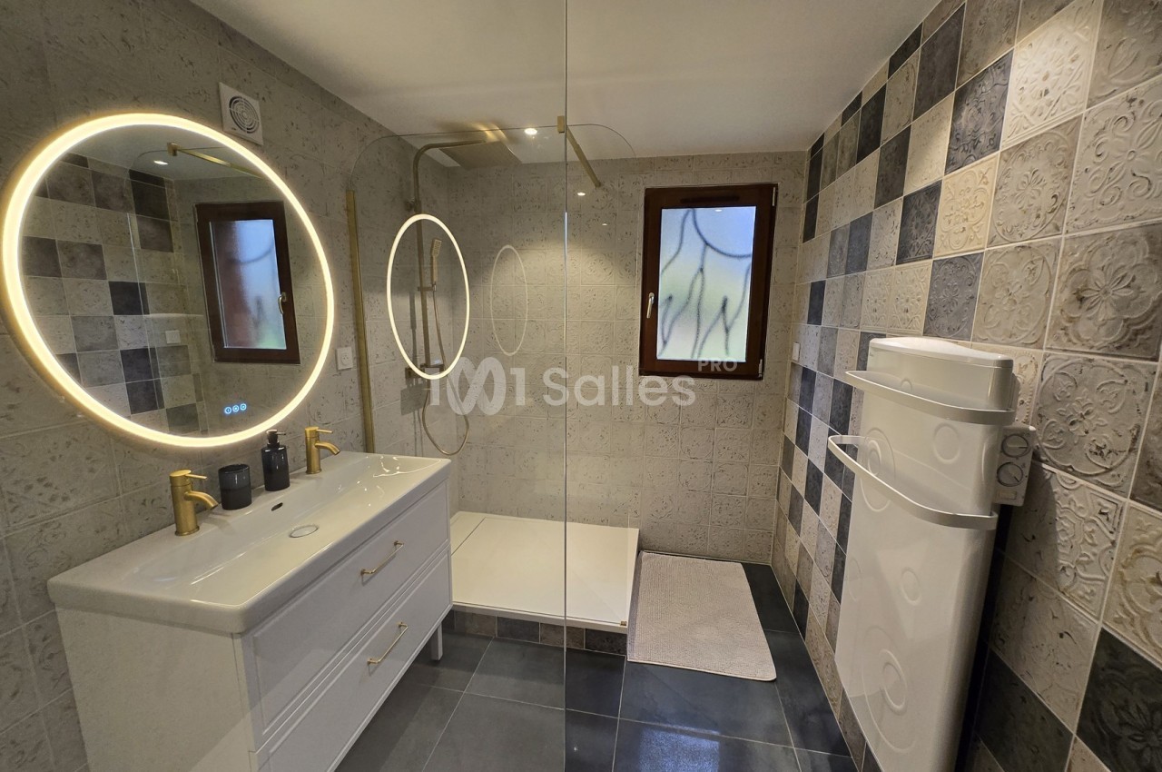 Salle de bain moderne avec douche à l'italienne, miroir rond lumineux, meuble double vasque et carrelage décoratif.