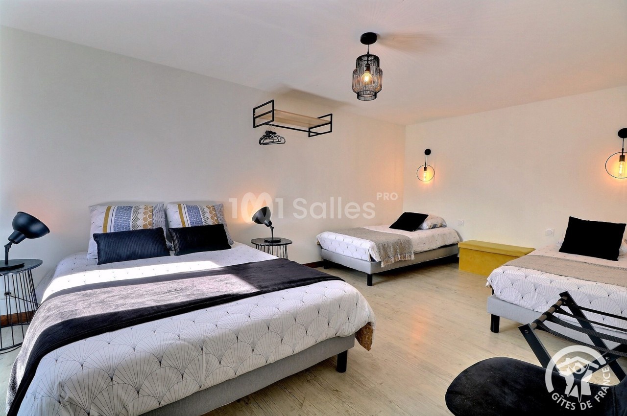 Chambre lumineuse avec trois lits, décor moderne, lampes suspendues et mobilier minimaliste.