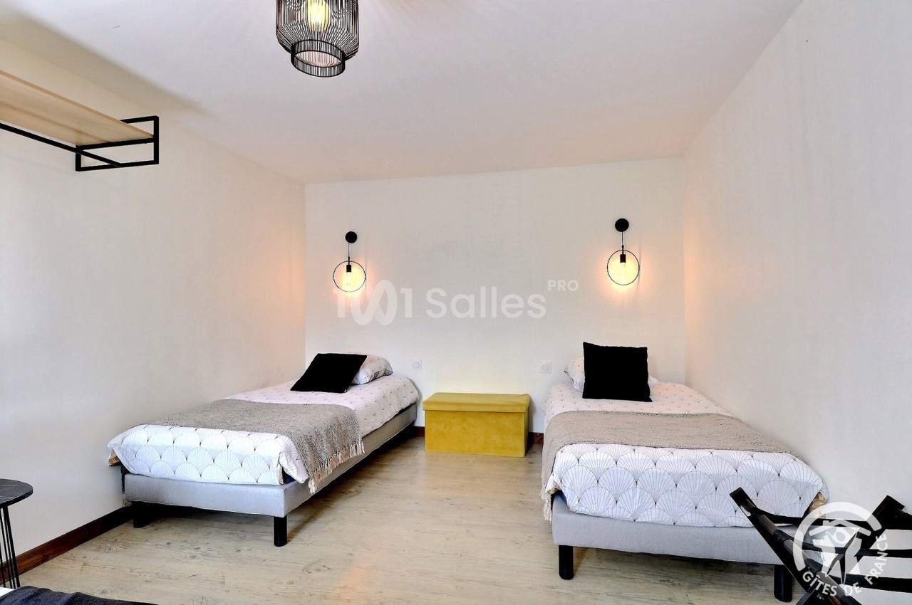 Deux lits simples avec linge de lit clair, éclairés par des appliques murales dans une chambre sobre et lumineuse.