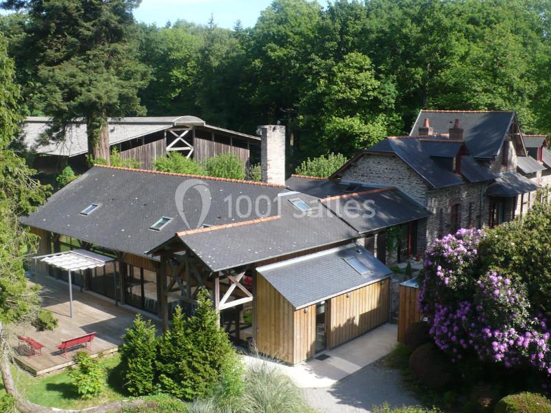 Bâtiments en pierre et bois entourés de végétation, avec toits en ardoise et jardin fleuri.