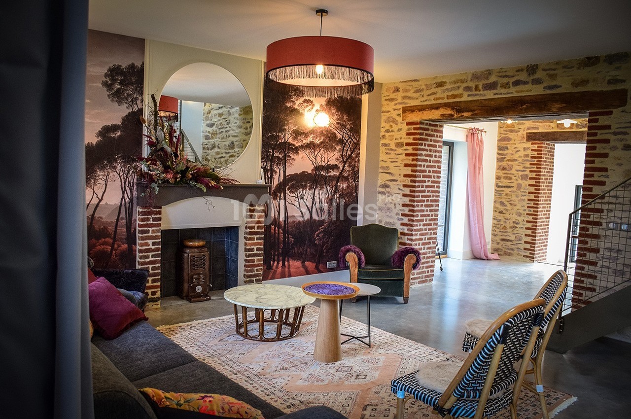 Salon chaleureux avec murs en pierre et briques, cheminée décorée, mobilier éclectique et grande ouverture lumineuse.