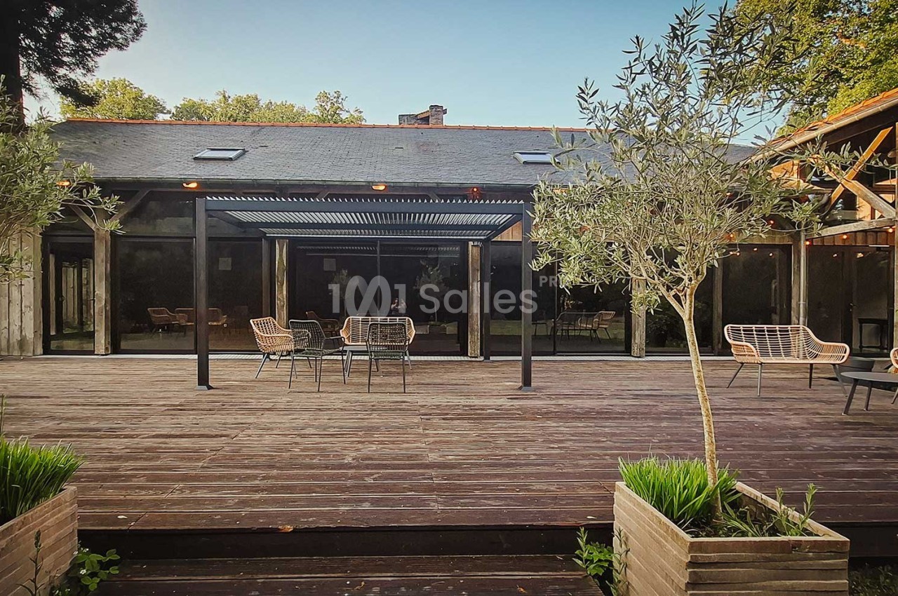 Terrasse en bois avec mobilier de jardin, pergola moderne et végétation environnante devant un bâtiment vitré.
