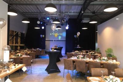 Salle décorée pour un anniversaire avec ballons noirs et dorés, tables dressées et une scène en fond.