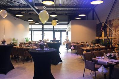 Salle décorée pour un anniversaire avec ballons noirs et dorés, tables dressées et une scène en fond.