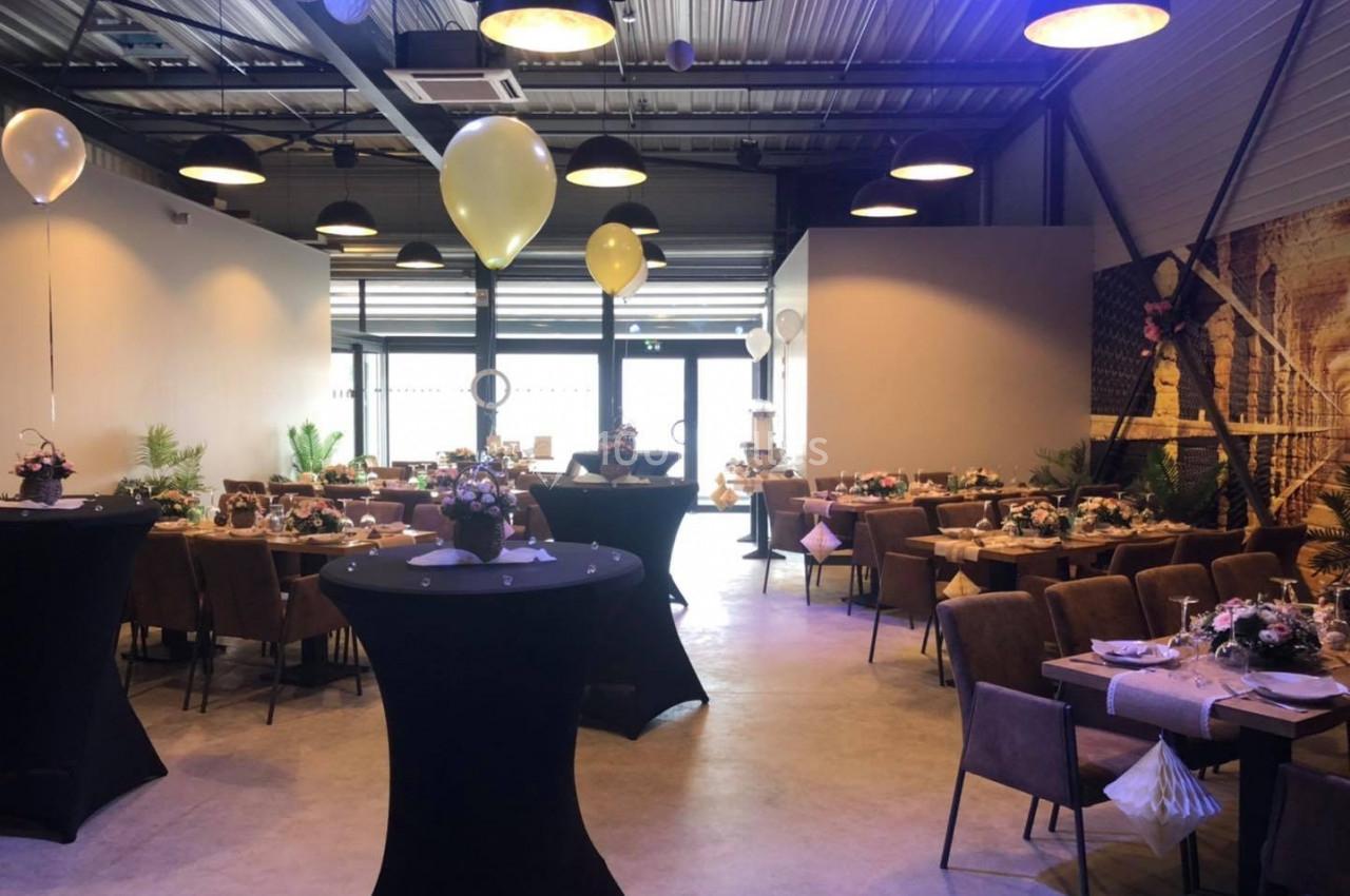 Salle décorée pour un événement avec tables dressées, ballons suspendus et éclairage tamisé.