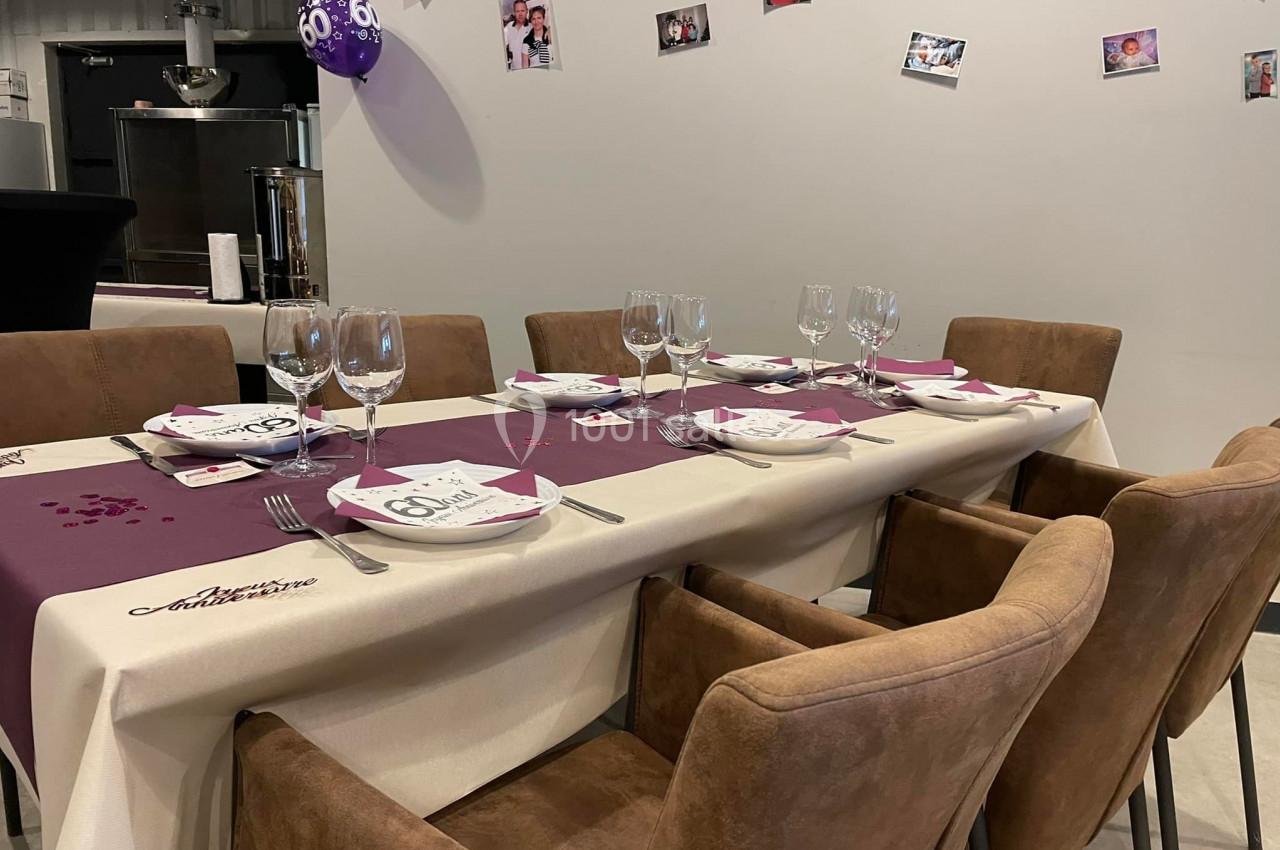 Table décorée pour une fête avec nappes, verres, assiettes et ballons, dans une salle ornée de photos au mur.
