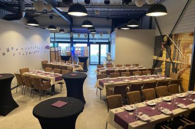 Salle décorée pour un anniversaire avec ballons noirs et dorés, tables dressées et une scène en fond.