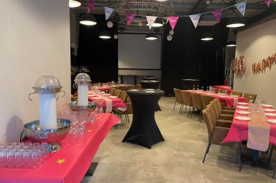 Salle décorée pour un anniversaire avec ballons noirs et dorés, tables dressées et une scène en fond.