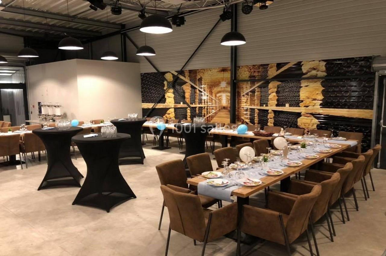 Salle décorée pour un événement avec tables dressées, chaises en cuir, mange-debout et éclairage suspendu.
