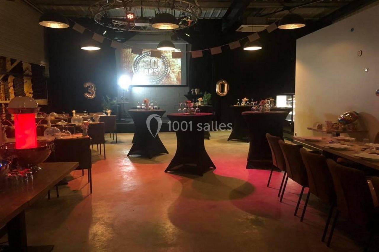 Salle décorée pour une fête d'anniversaire avec tables hautes, guirlandes et projection lumineuse ’30 ans’.