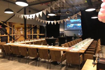 Salle décorée pour un anniversaire avec ballons noirs et dorés, tables dressées et une scène en fond.