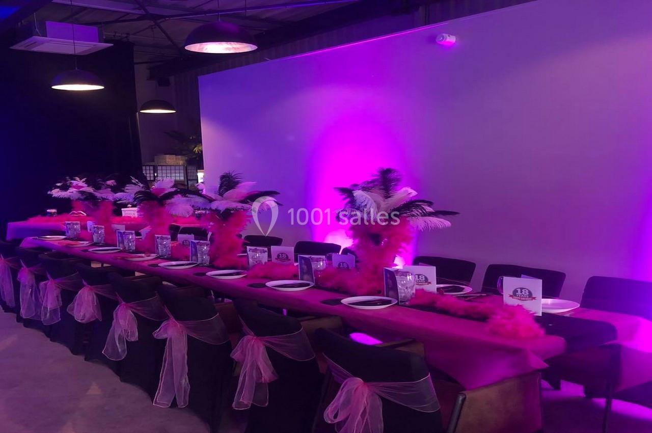 Table décorée avec des nappes roses, plumes blanches et noires, et chaises ornées de rubans roses dans une ambiance…