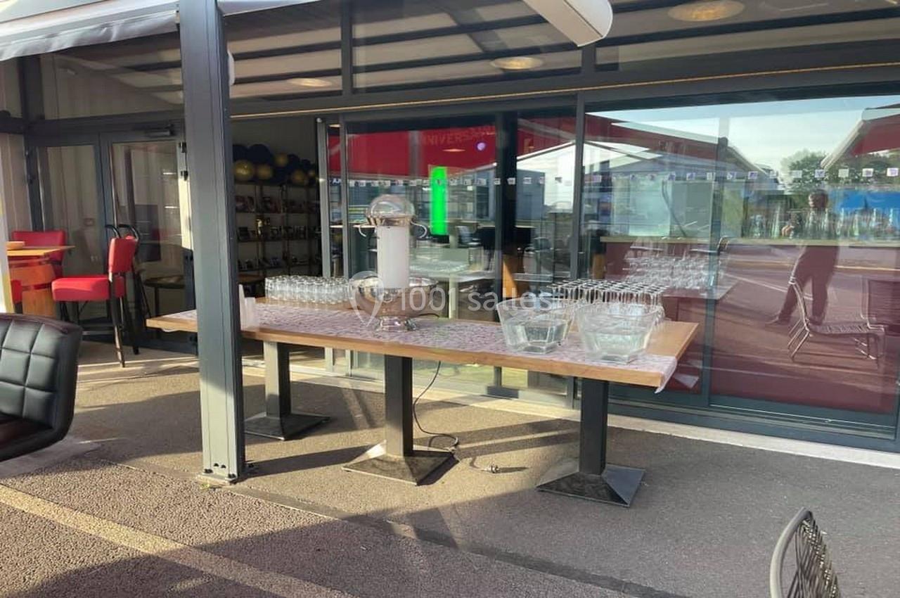 Table en extérieur avec verres alignés et seau à glaçons, située près d'une baie vitrée d'un espace couvert.