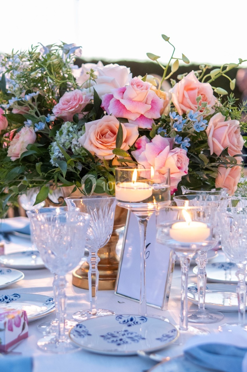 Centre de table floral avec roses et bougies allumées, entouré de vaisselle en porcelaine blanche et bleue.