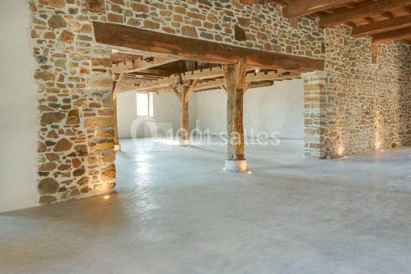 Intérieur d'une grande pièce avec murs en pierre apparente, poutres en bois et sol en béton poli.