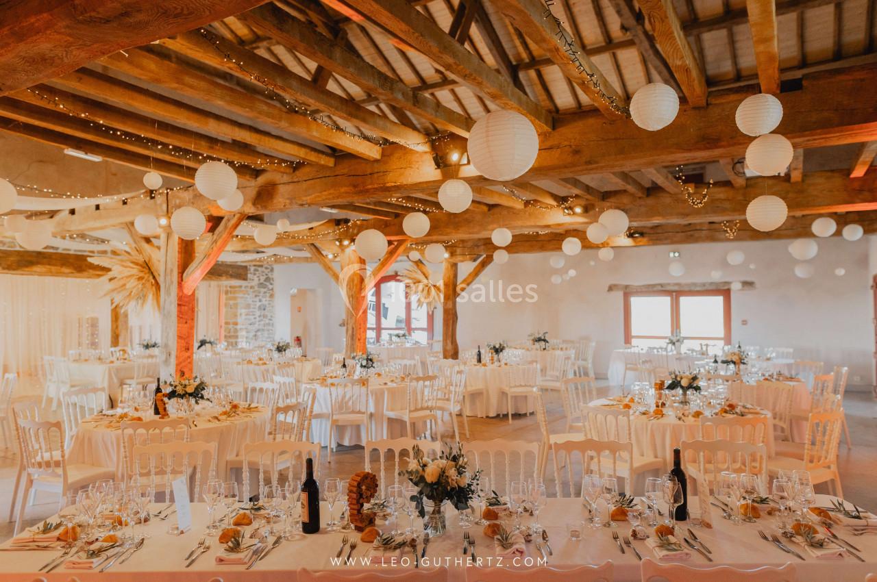 Salle de réception décorée avec des guirlandes lumineuses, des lanternes suspendues et des tables dressées pour un événement.