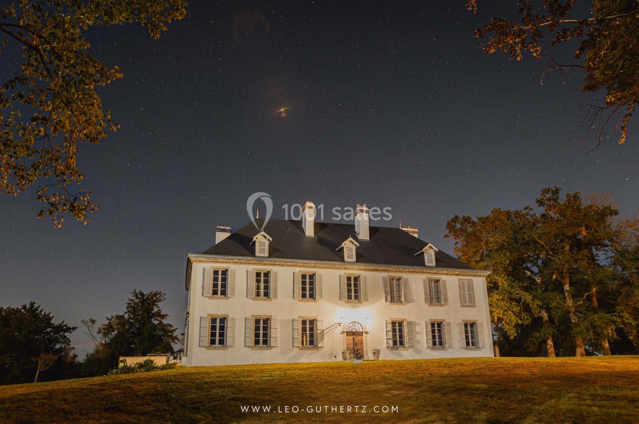 Manoir blanc éclairé la nuit, entouré d'arbres, sous un ciel étoilé.