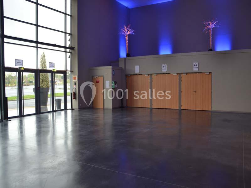 Location salle Dammarie-les-Lys (Seine-et-Marne) - Espace Pierre Bachelet #22 Hall d'entrée spacieux avec sol en béton, portes en bois, grandes fenêtres et éclairage bleu décoratif.