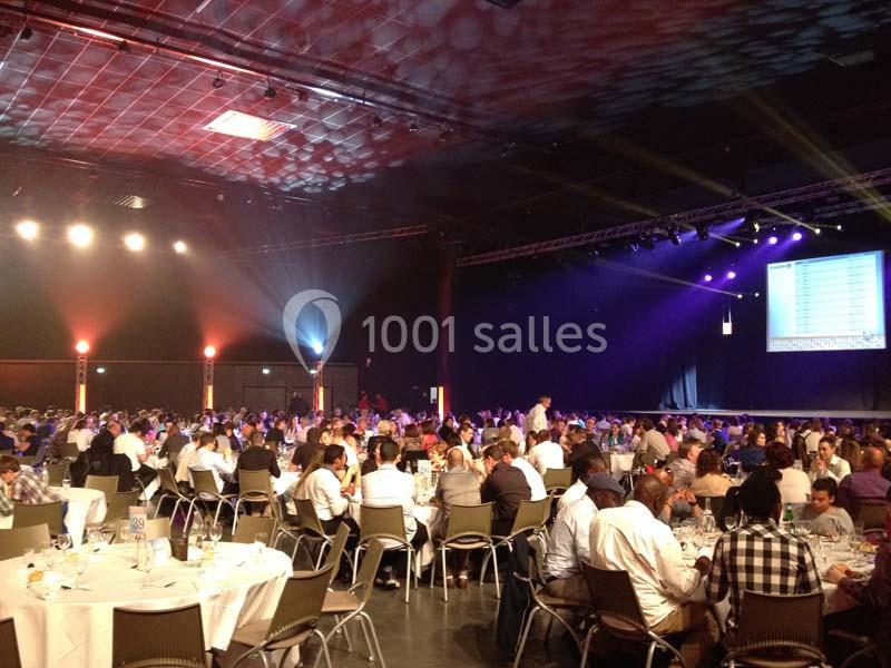 Location salle Dammarie-les-Lys (Seine-et-Marne) - Espace Pierre Bachelet #12 Salle de réception remplie de tables rondes avec des convives, éclairée par des projecteurs et un écran en fond.