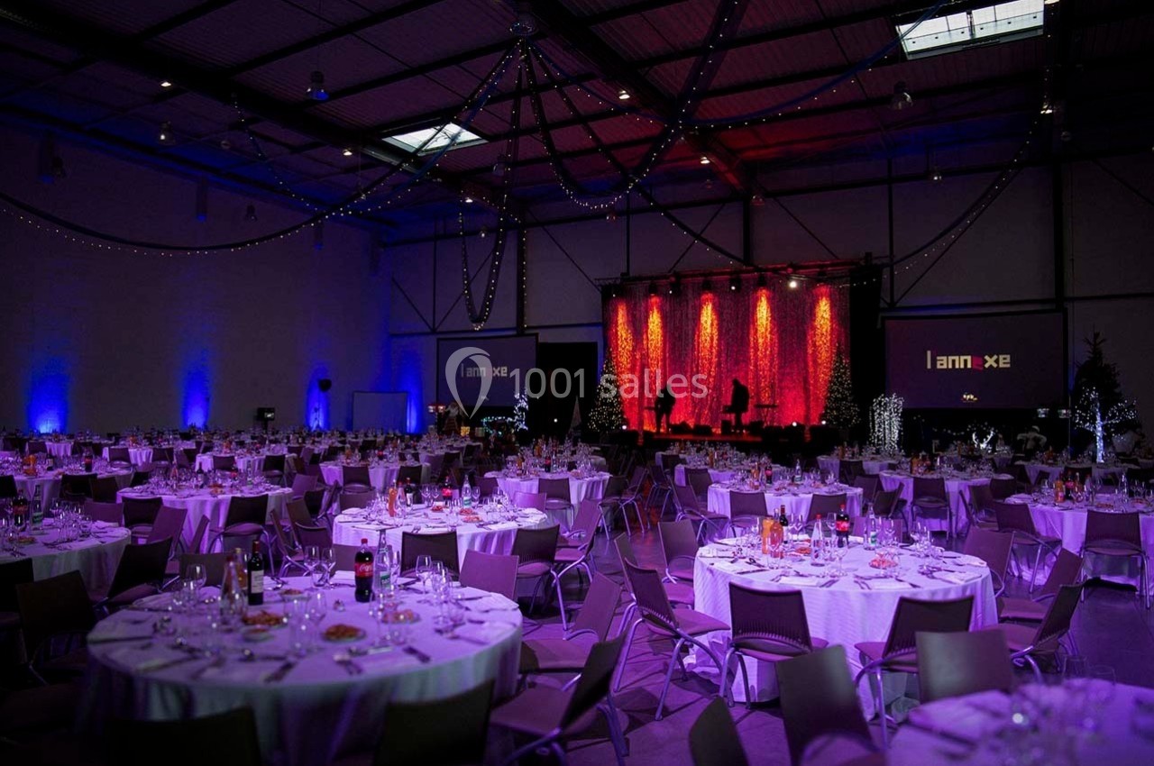 Location salle Dammarie-les-Lys (Seine-et-Marne) - Espace Pierre Bachelet #1 Salle de réception décorée avec des tables rondes dressées, éclairage tamisé et scène illuminée en arrière-plan.