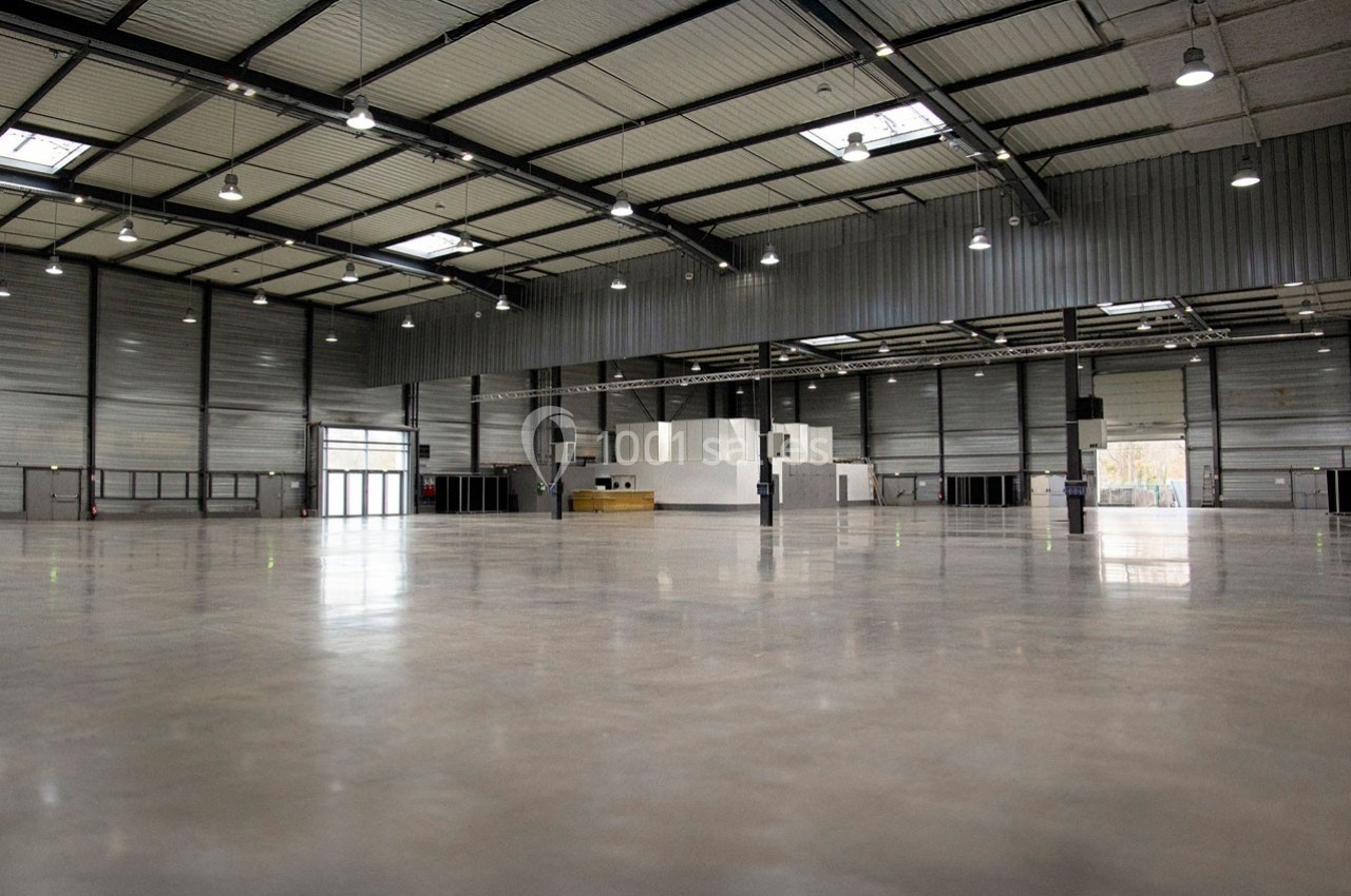 Location salle Dammarie-les-Lys (Seine-et-Marne) - Espace Pierre Bachelet #5 Intérieur d'un grand entrepôt vide avec sol en béton poli, murs métalliques et éclairage suspendu.