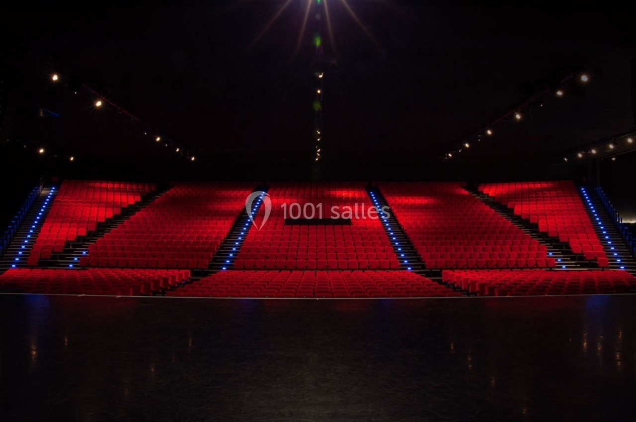 Salle de spectacle vide avec rangées de sièges rouges et éclairage tamisé, escalier central illuminé.