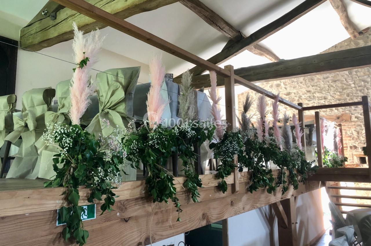 Décoration florale avec feuillage, gypsophile et herbes de la pampa sur une rambarde en bois dans une salle rustique.
