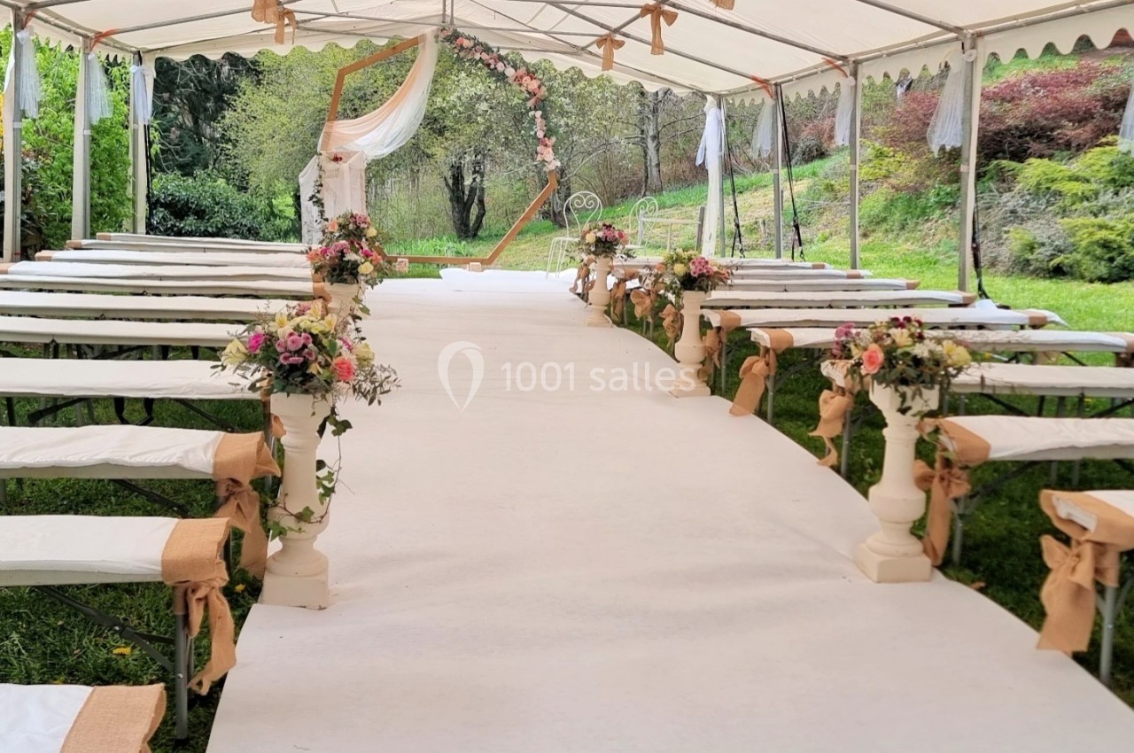 Allée centrale décorée de fleurs sous une tente blanche, préparée pour une cérémonie en extérieur.
