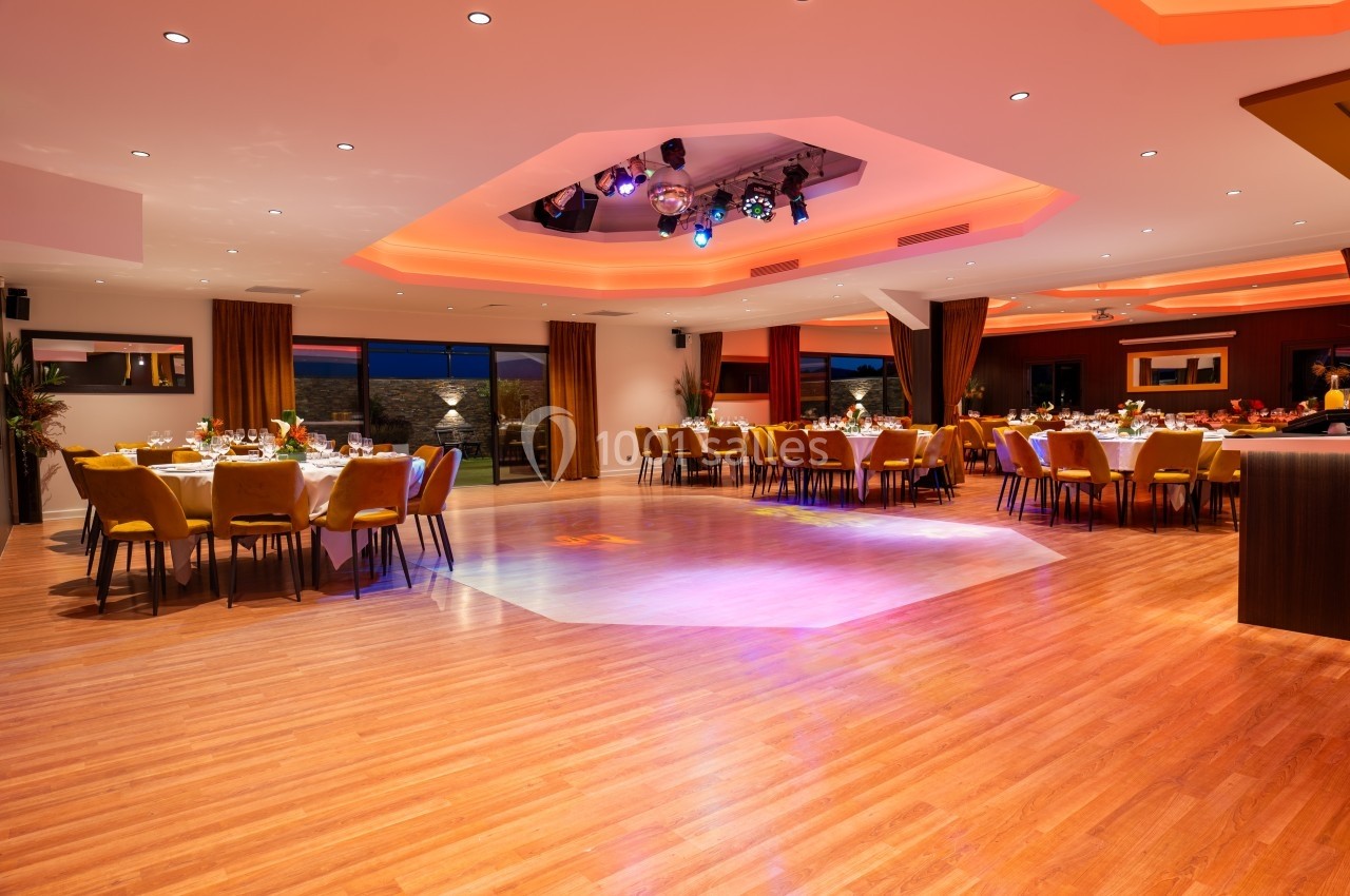 Salle de réception spacieuse avec parquet, tables dressées, éclairage chaleureux et piste de danse centrale.