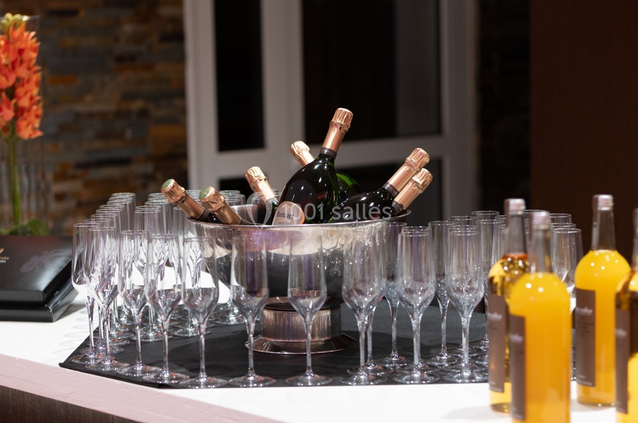 Seau rempli de bouteilles de champagne entouré de flûtes en verre et de bouteilles de liqueur sur un comptoir.