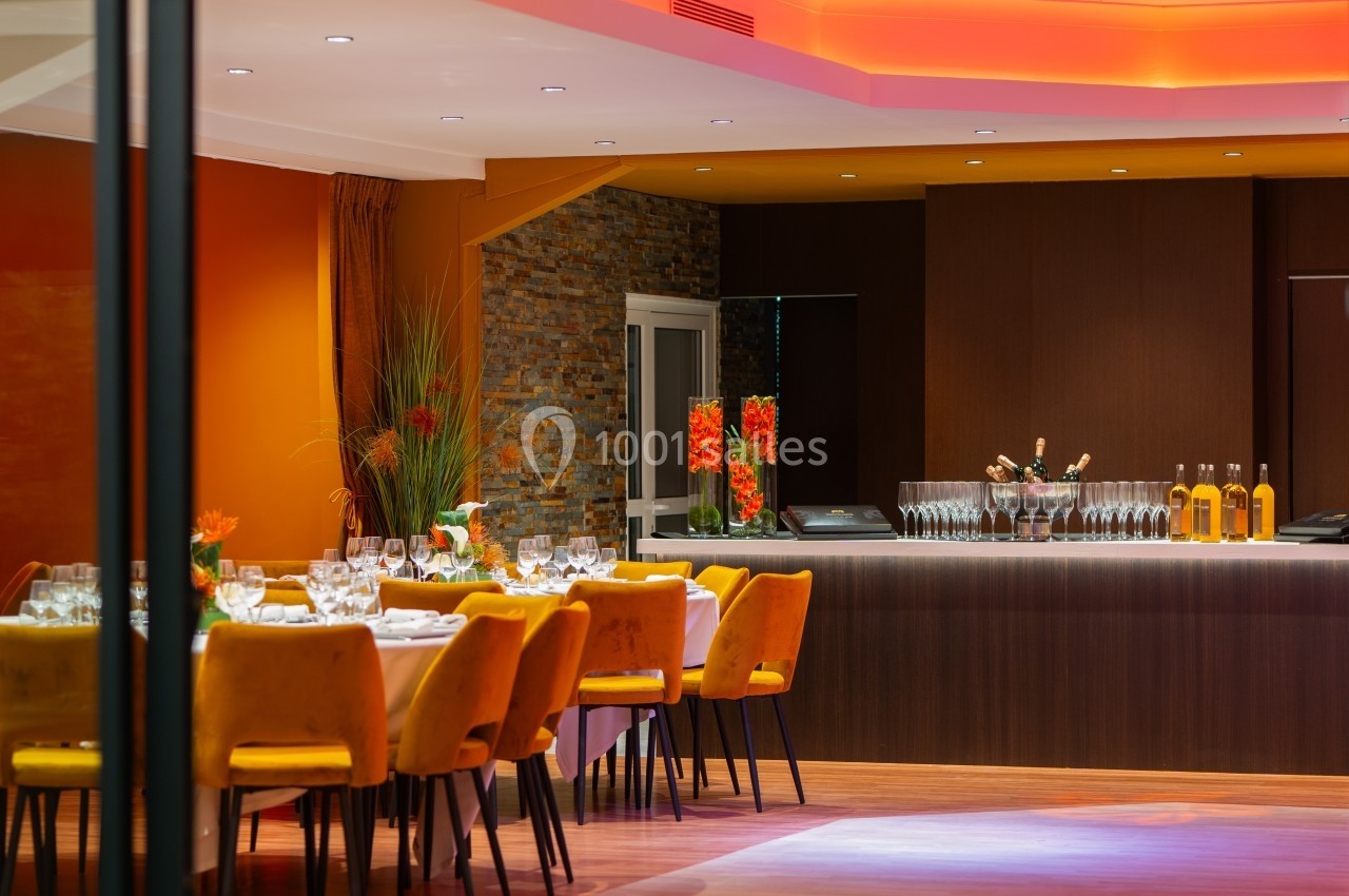 Salle de restaurant élégante avec tables dressées, chaises jaunes et bar en arrière-plan sous un éclairage chaleureux.