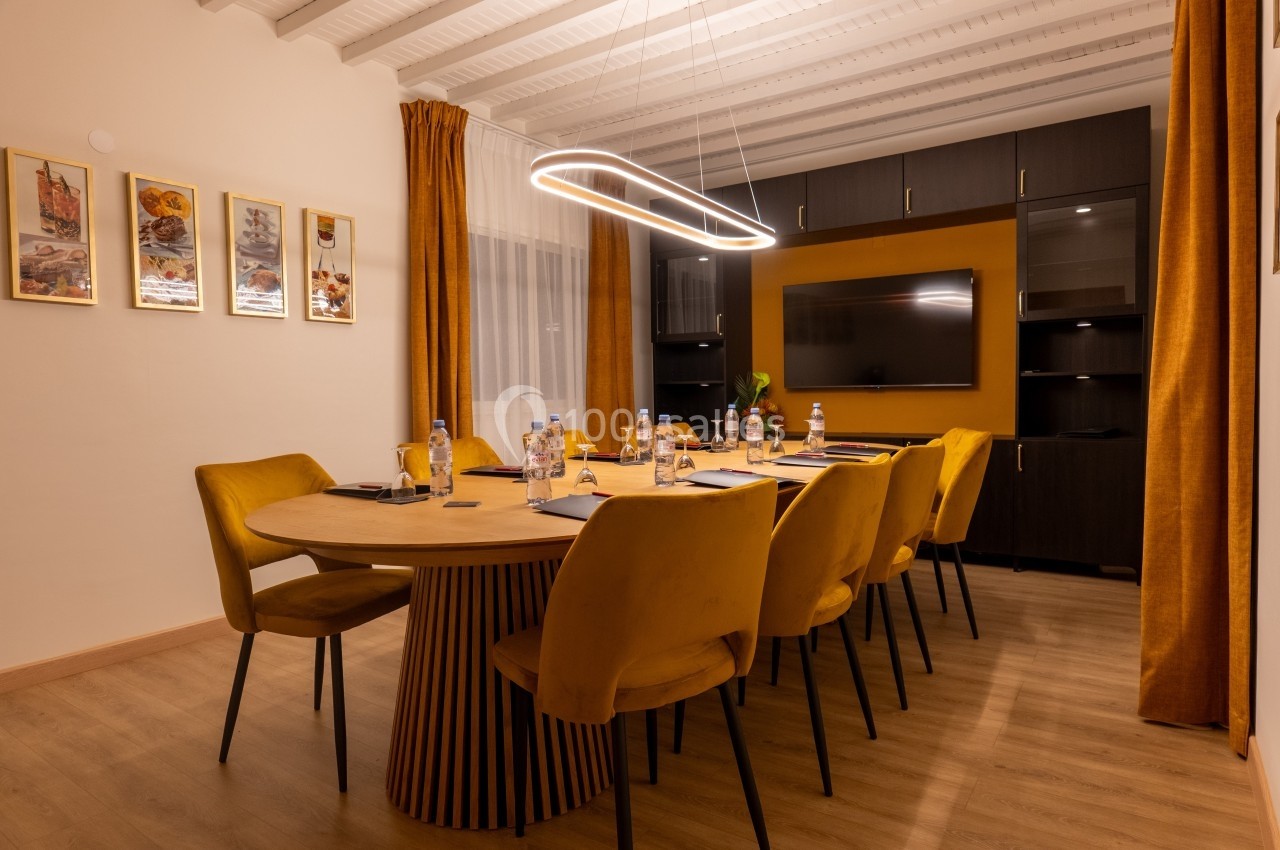 Salle de réunion moderne avec table ronde, chaises jaunes, écran mural et éclairage suspendu.
