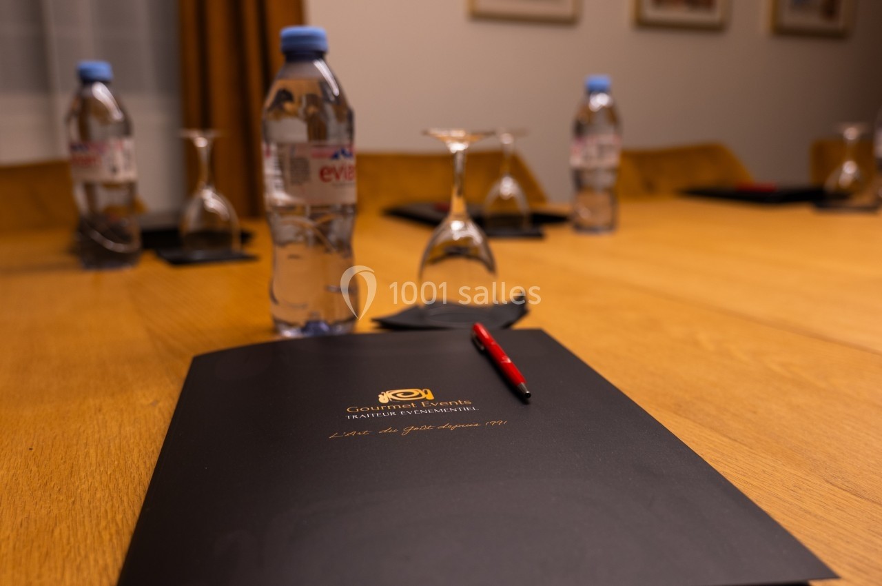 Bloc-notes noir avec un stylo rouge sur une table de réunion en bois, entourée de bouteilles d'eau et de verres.