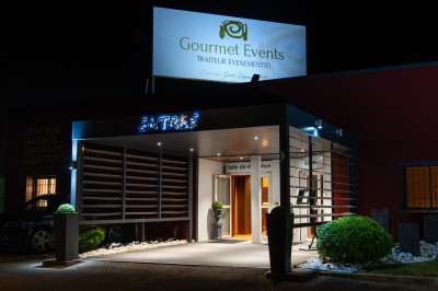 Miniature Location salle Sainte-Consorce (Rhône) - Gourmet Events #16 Façade éclairée d'un bâtiment abritant un traiteur événementiel, avec un panneau lumineux et une entrée visible.