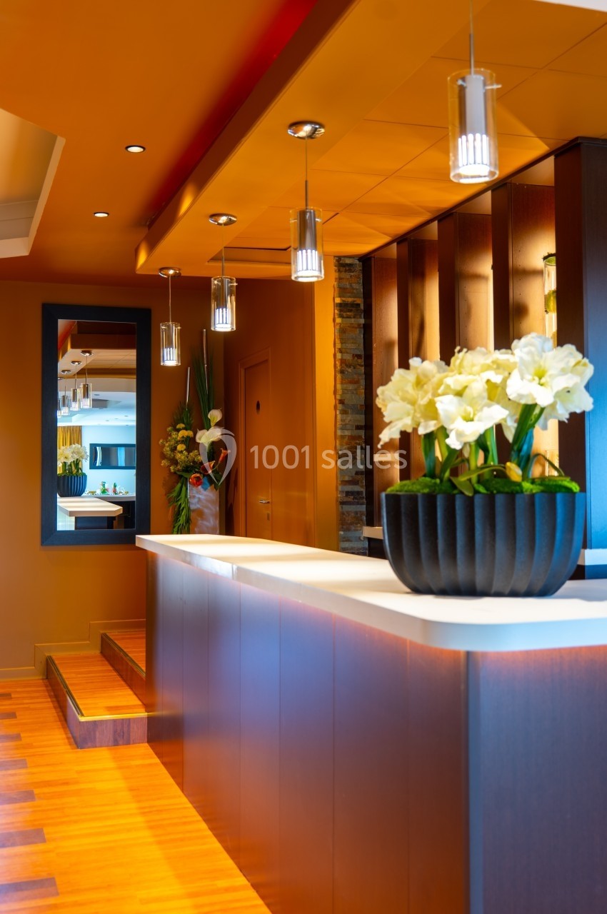 Comptoir moderne en bois avec éclairage suspendu, décoré de fleurs blanches dans un vase noir.