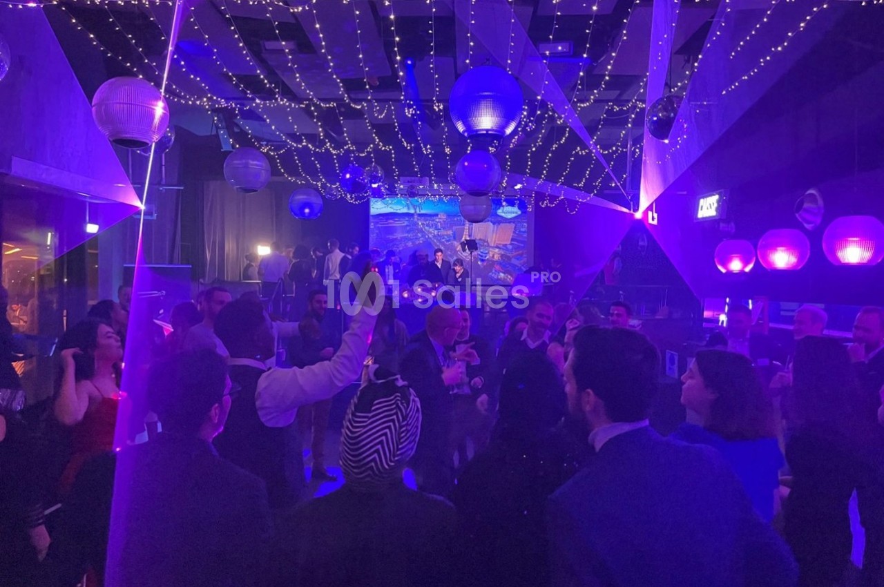 Personnes dansant sous des lumières colorées et des décorations suspendues dans une salle de fête animée.