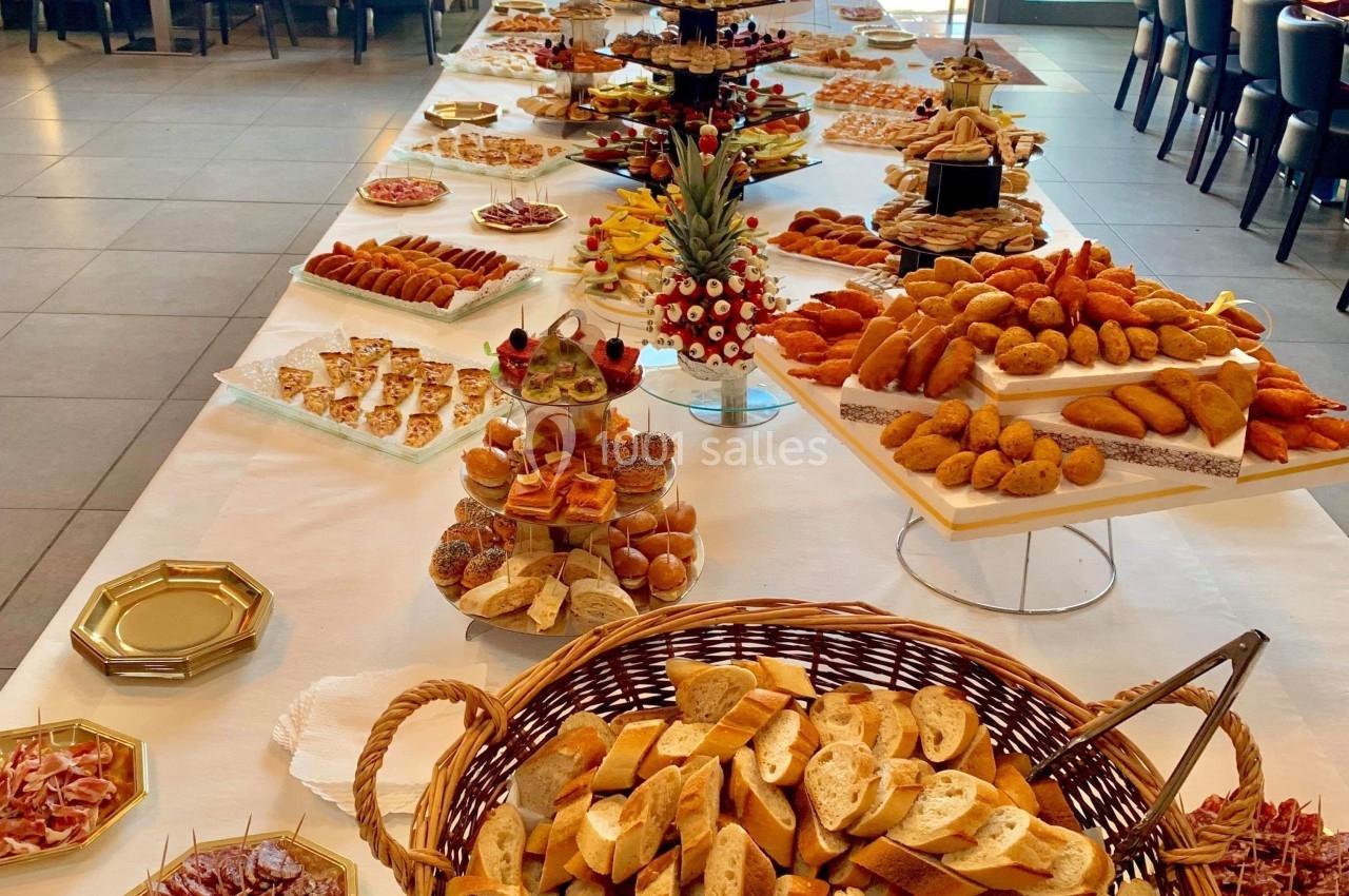 Table garnie d'un buffet varié comprenant pains, viennoiseries, charcuteries et desserts dans une salle lumineuse.
