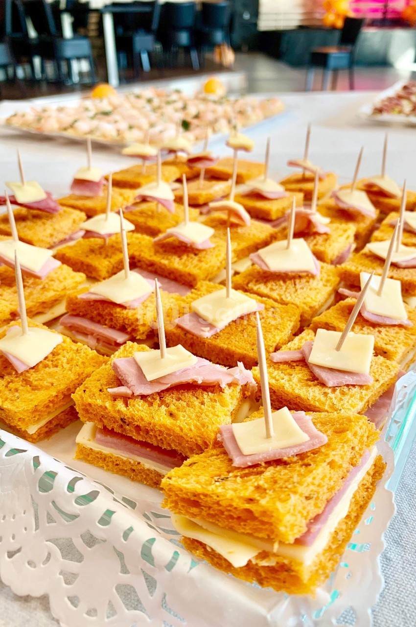 Assortiment de mini-sandwiches au pain de mie orange, garnis de fromage et jambon, présentés avec des pics en bois.