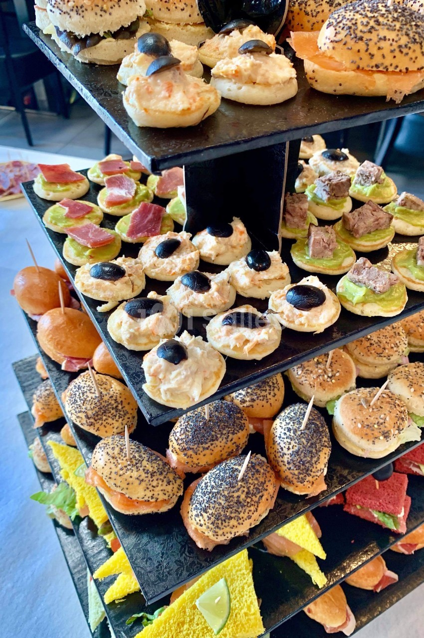 Plateau de bouchées apéritives variées disposées sur plusieurs étages, comprenant canapés, mini-burgers et toasts colorés.